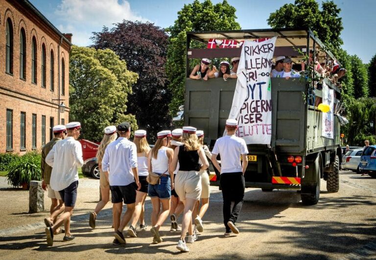 Glade studenter løber efter Nicedrive studentervogn, model 'Monster Truck 1', med deres studenterhuer på en studenterkørsel på en solrig dag, tilgængelig til en billig pris