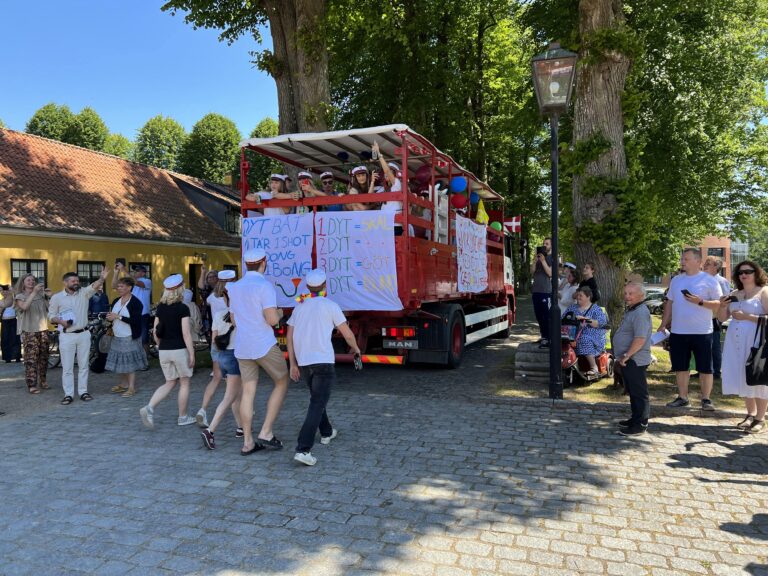 Glade studenter løber efter Nicedrive studentervogn, model 'Ølvognen', med deres studenterhuer på en studenterkørsel på en solrig dag, tilgængelig til en billig pris