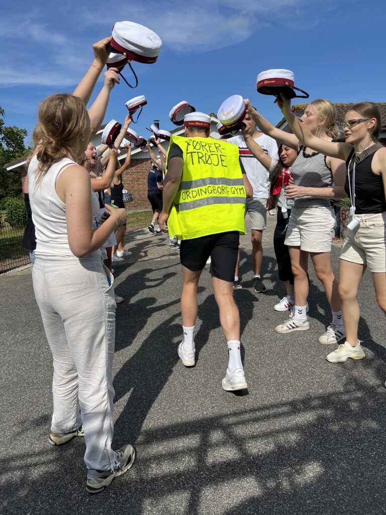 Glade studenter foran Nicedrive studentervogn, model 'Discovognen', danner espalier med deres studenterhuer på studenterkørsel på en solrig dag, tilgængelig til en billig pris