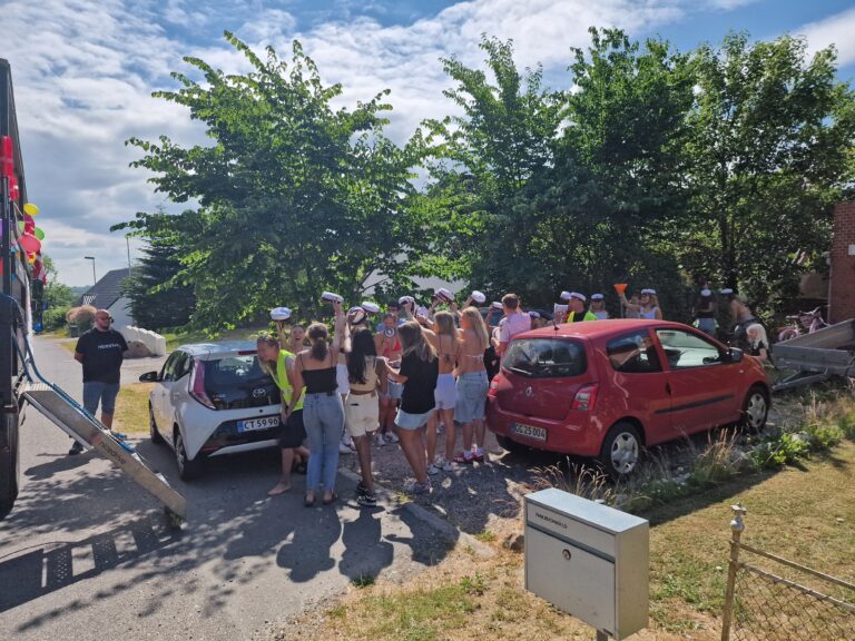 Glade studenter foran Nicedrive studentervogn, model 'Druk Dynamoen', danner espalier med deres studenterhuer på studenterkørsel på en solrig dag, tilgængelig til en billig pris