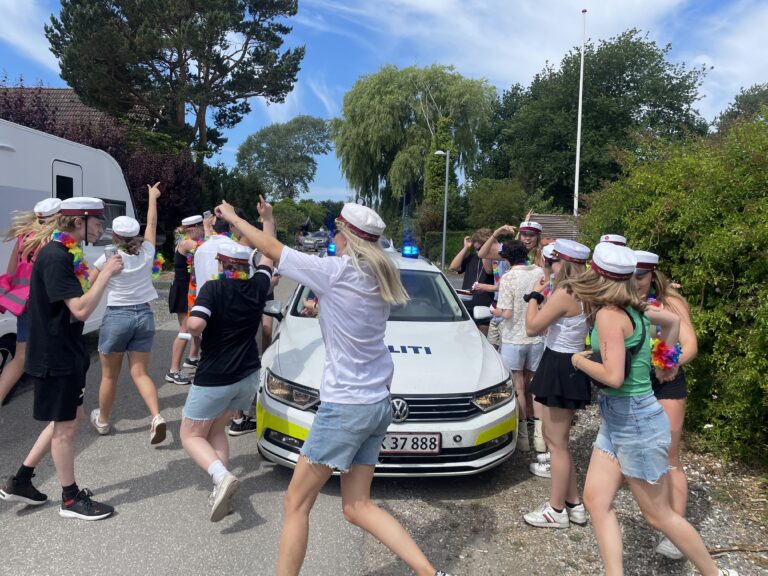 Glade studenter klar til festlig studenterkørsel i Nicedrive studentervogn, model 'Druk Dynamoen', dekoreret med bannere og danske flag, tilgængelig til en billig pris