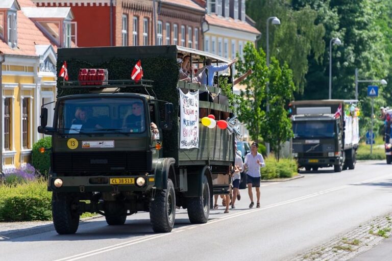 Glade studenter løber efter Nicedrive studentervogn, model 'Monster Truck 1', med deres studenterhuer på en studenterkørsel på en solrig dag, tilgængelig til en billig pris