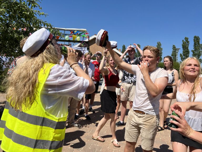 Glade studenter foran Nicedrive studentervogn, model 'Party Piraten', danner espalier med deres studenterhuer på studenterkørsel på en solrig dag, tilgængelig til en billig pris