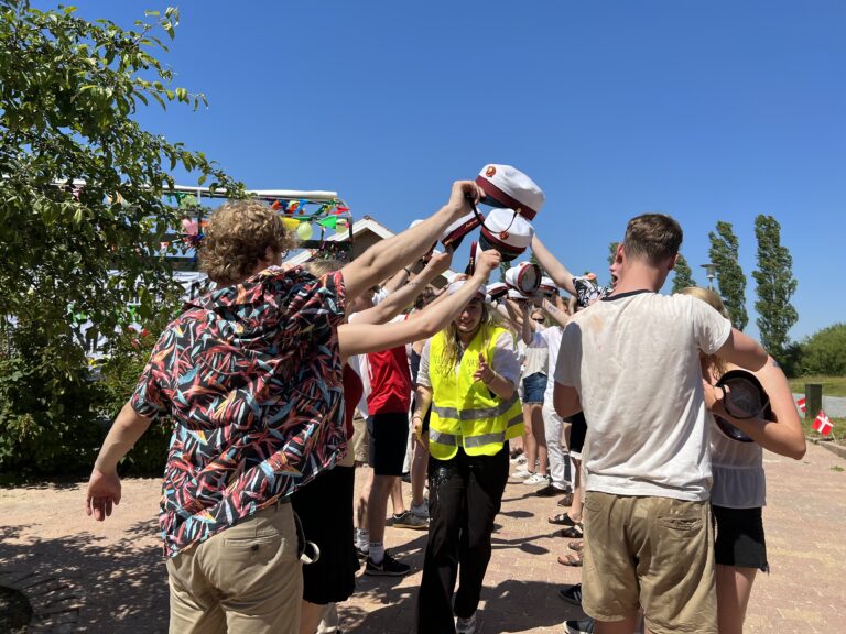 Glade studenter foran Nicedrive studentervogn, model 'Party Piraten', danner espalier med deres studenterhuer på studenterkørsel på en solrig dag, tilgængelig til en billig pris