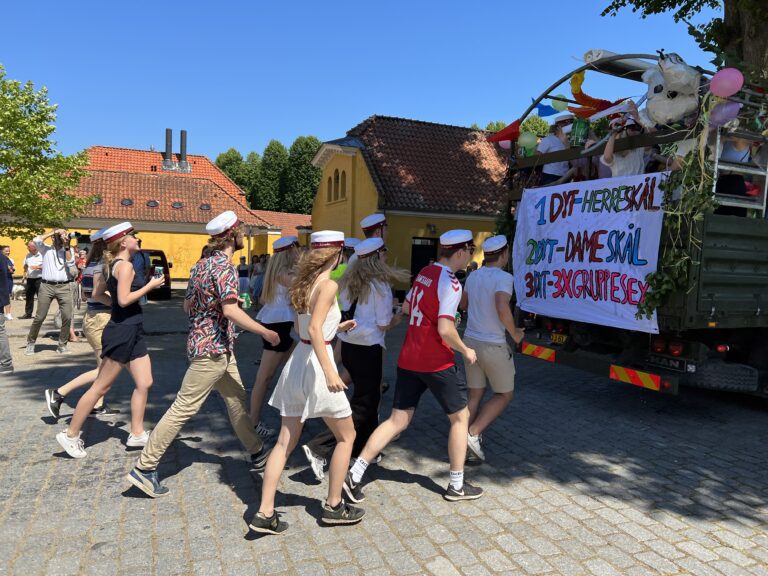 Glade studenter løber efter Nicedrive studentervogn, model 'Young Party', med deres studenterhuer på en studenterkørsel på en solrig dag, tilgængelig til en billig pris