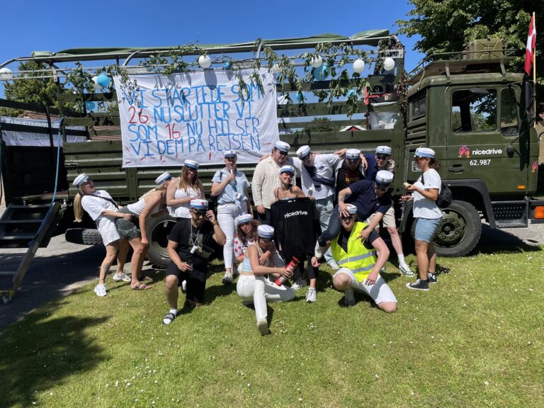 Glade studenter klar til festlig studenterkørsel i Nicedrive studentervogn, model ‘Stripperstangen’, dekoreret med bannere og danske flag, tilgængelig til en billig pris