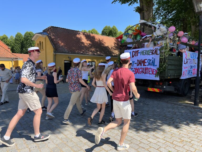 Glade studenter løber efter Nicedrive studentervogn, model ‘Powershot’, med deres studenterhuer på en studenterkørsel på en solrig dag, tilgængelig til en billig pris